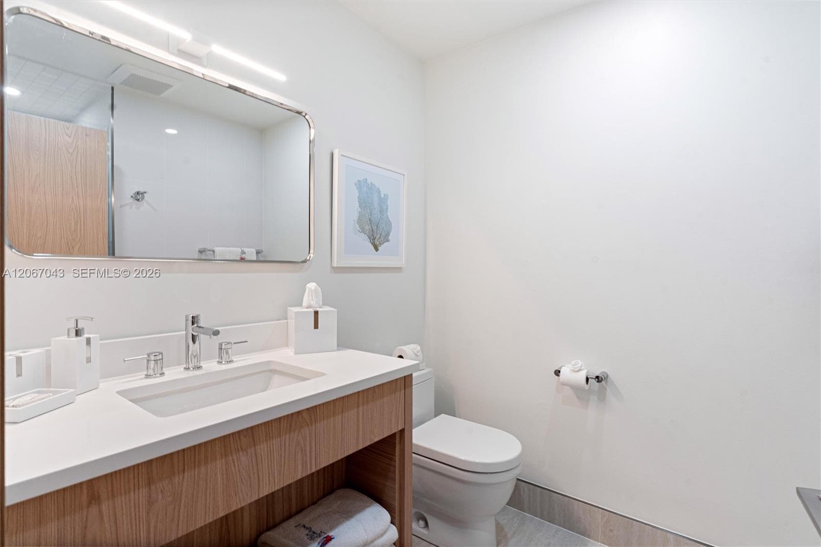 Wood-finish vanity with a rectangular sink, white composite countertop, polished chrome widespread faucet, and large rectangular mirror with an integrated light bar