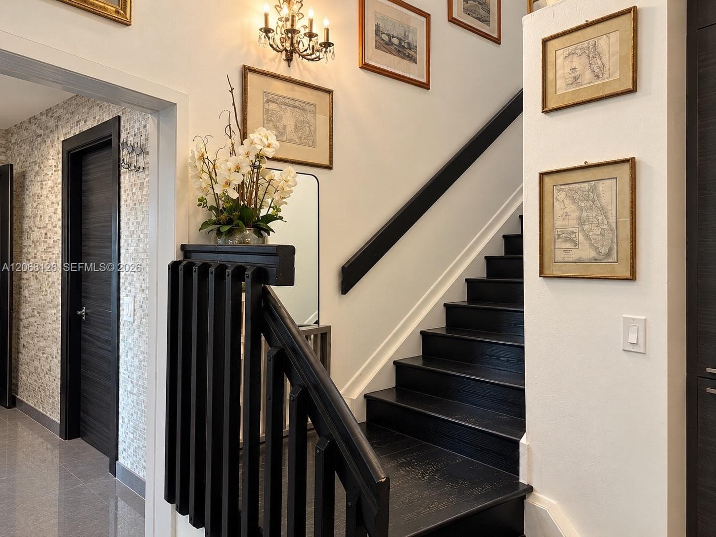 Staircase featuring dark-stained wood treads, a matching handrail, and a decorative balustrade, complemented by wall-mounted sconce lighting and textured wall accents
