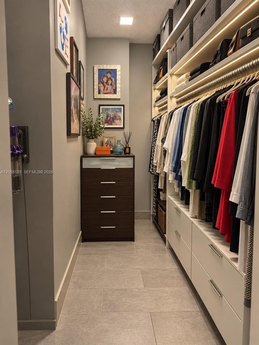 Custom walk-in closet featuring extensive built-in white cabinetry, integrated LED shelf lighting, polished metal hanging rods, and large-format tile flooring