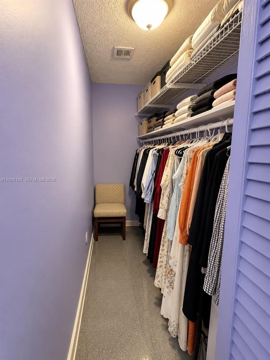 Walk-in closet featuring tiered wire shelving, mounted garment rods, and solid-surface flooring