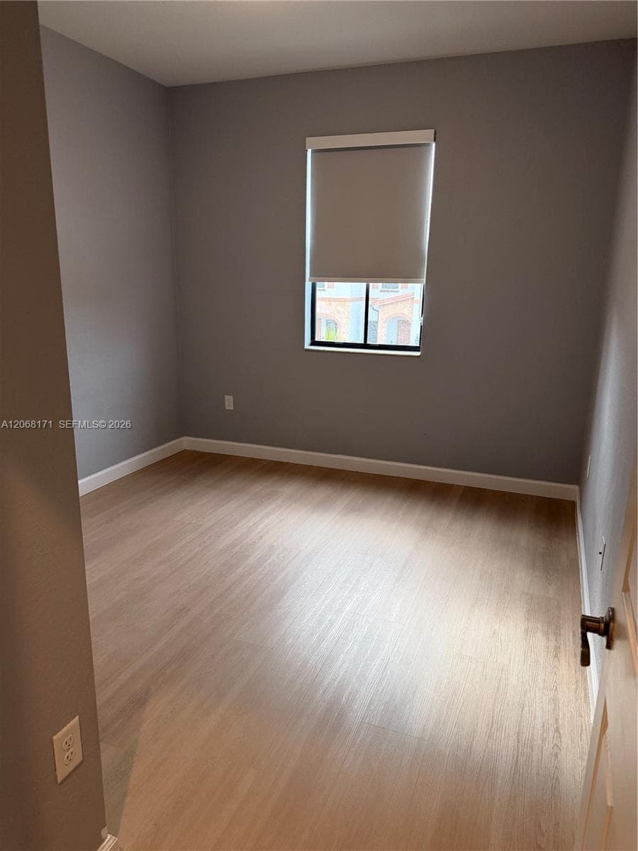 Interior room featuring neutral wall paint, wood-finish flooring, and a single window with a roller shade