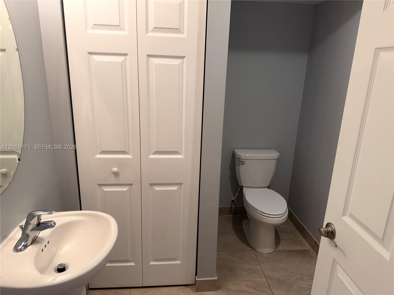Powder room featuring a pedestal sink, chrome faucet, white bifold closet doors, two-piece toilet, and tile flooring
