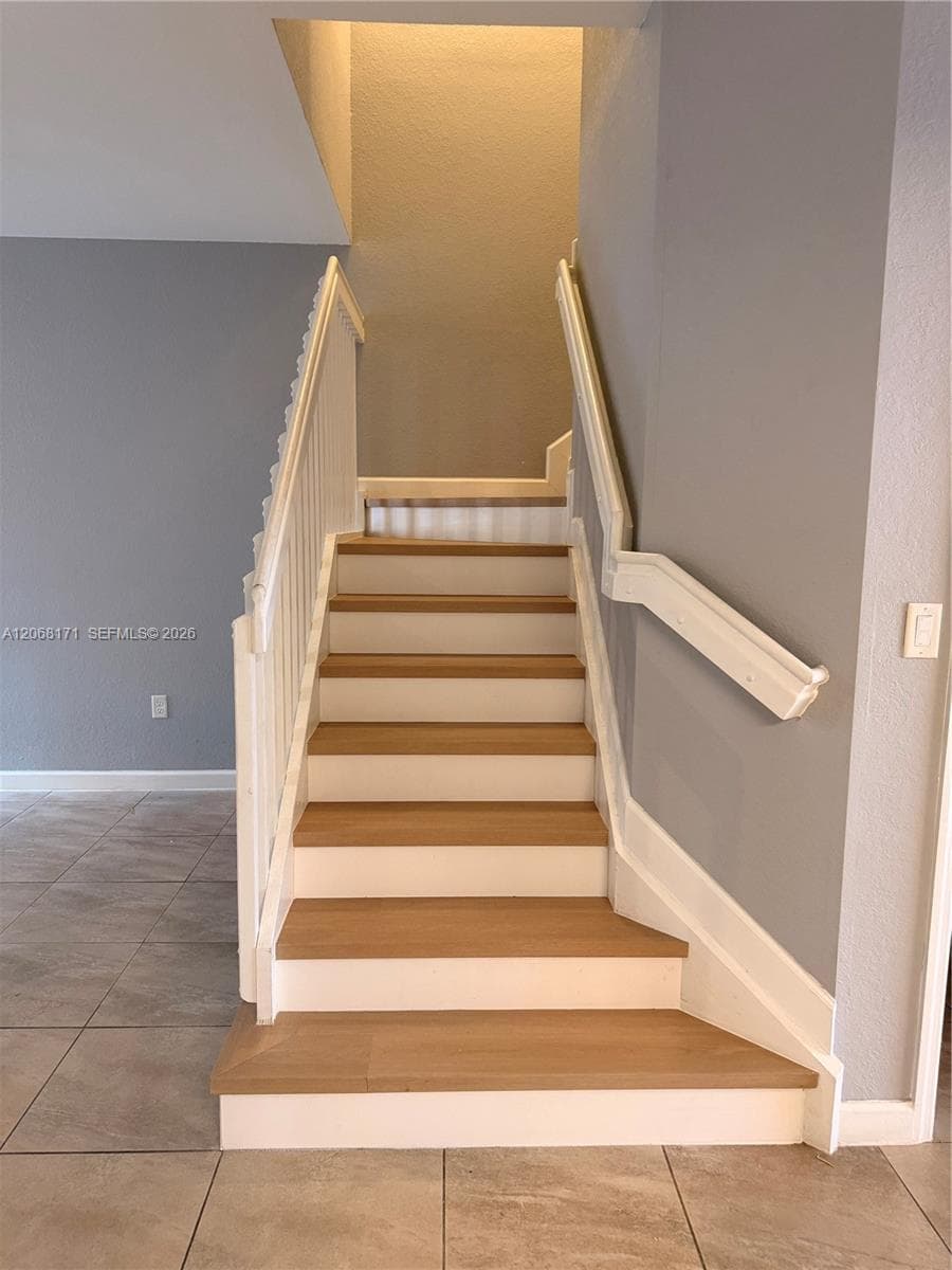 Staircase featuring wood-finish treads, white risers, a white spindle railing, and a wall-mounted handrail