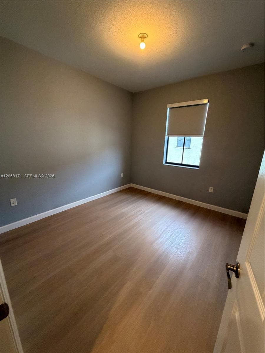 Neutral-toned walls paired with light-toned wood-finish flooring, a single-pane window with a roller shade, and a centered dome ceiling light fixture