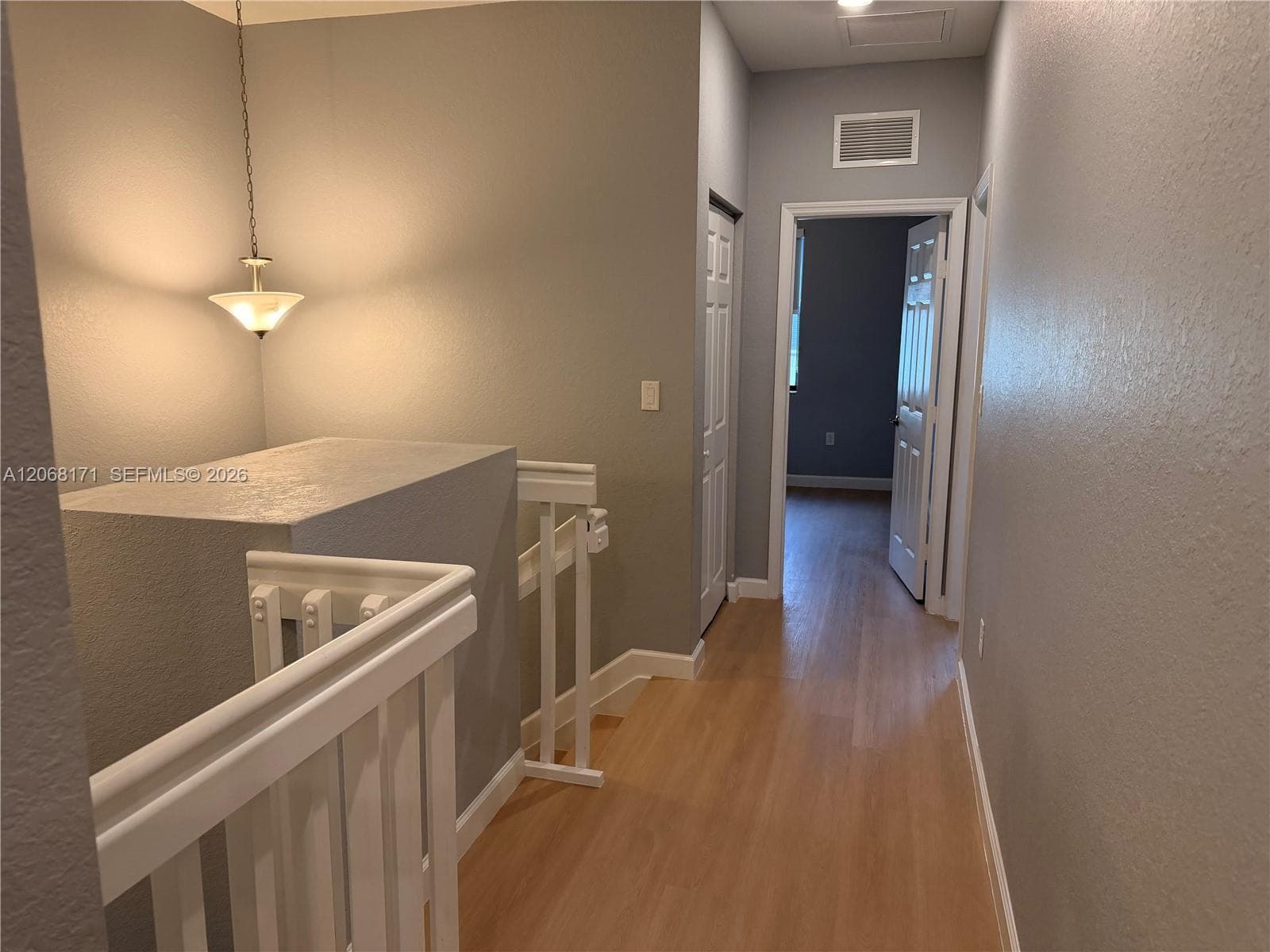 Hallway featuring wood-finish flooring, white railing with square balusters, a ceiling-mounted pendant light, and six-panel interior doors