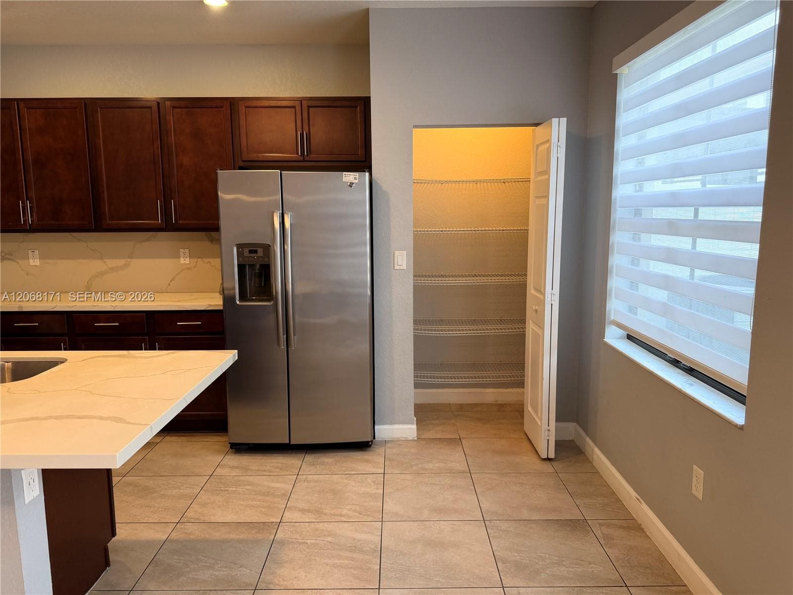 Kitchen featuring dark-finish cabinetry, stone-surface countertops with backsplash, stainless steel refrigerator, tile flooring, and walk-in pantry with wire shelving