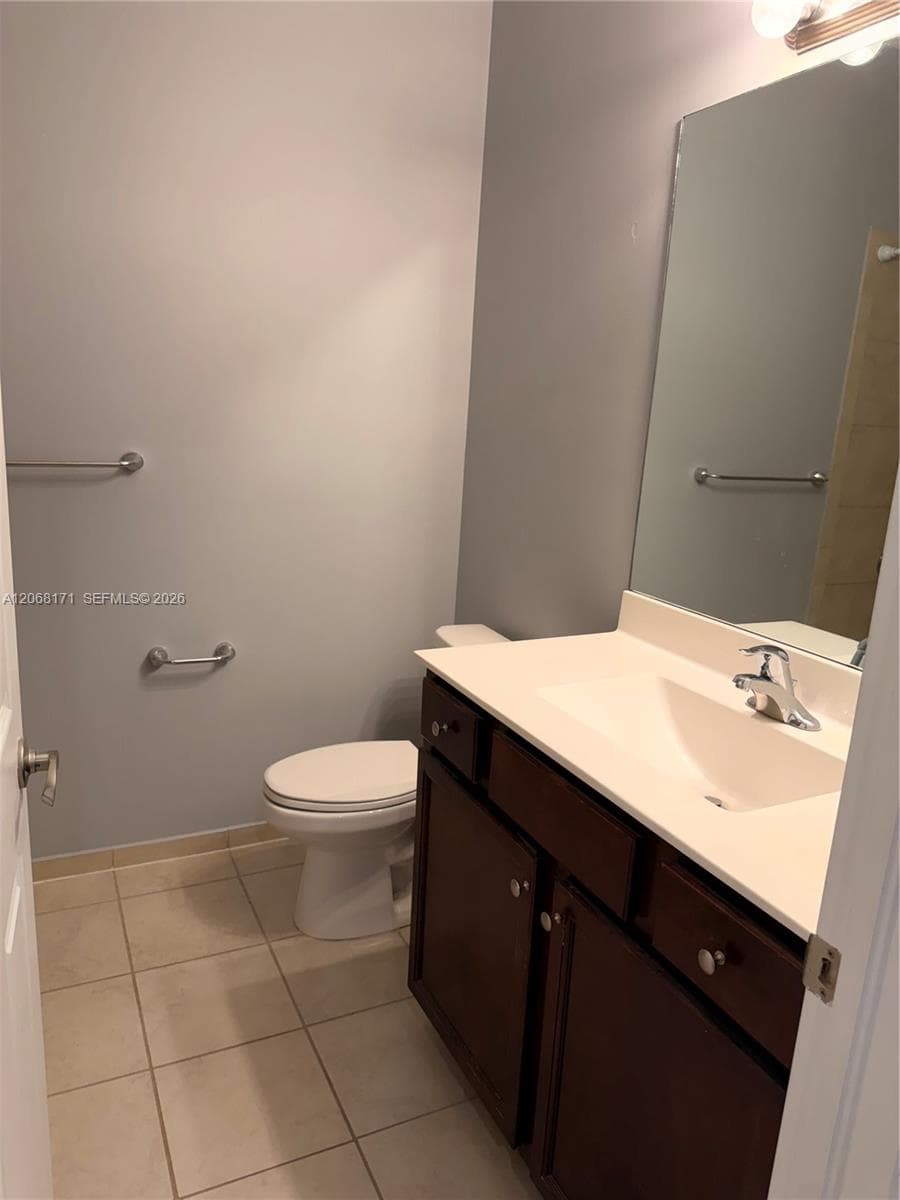 Bathroom featuring a vanity with a white countertop and integrated basin, dark wood-finish cabinetry, ceramic tile flooring, and a full-height wall mirror