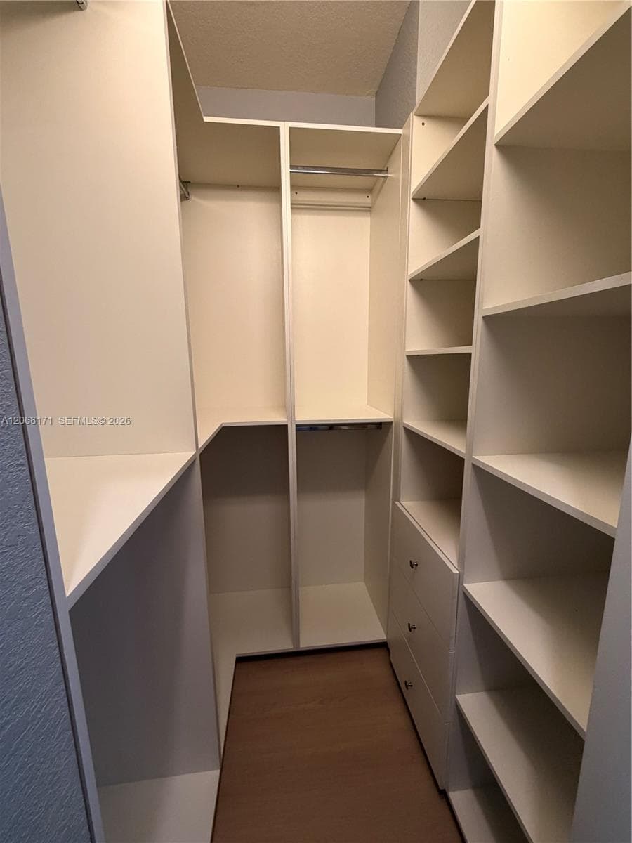 Walk-in closet featuring white built-in shelving, integrated dresser drawers with metallic hardware, and multiple hanging rods