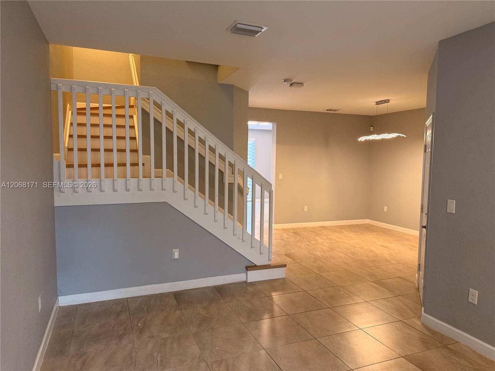 Open floor plan featuring tile flooring, a staircase with white vertical balusters and handrails, and a modern tiered pendant light fixture