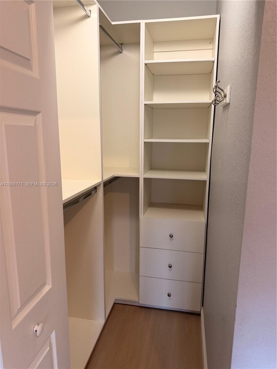 Custom walk-in closet featuring white built-in shelving, multiple hanging rods, a three-drawer storage unit, and wood-finish flooring