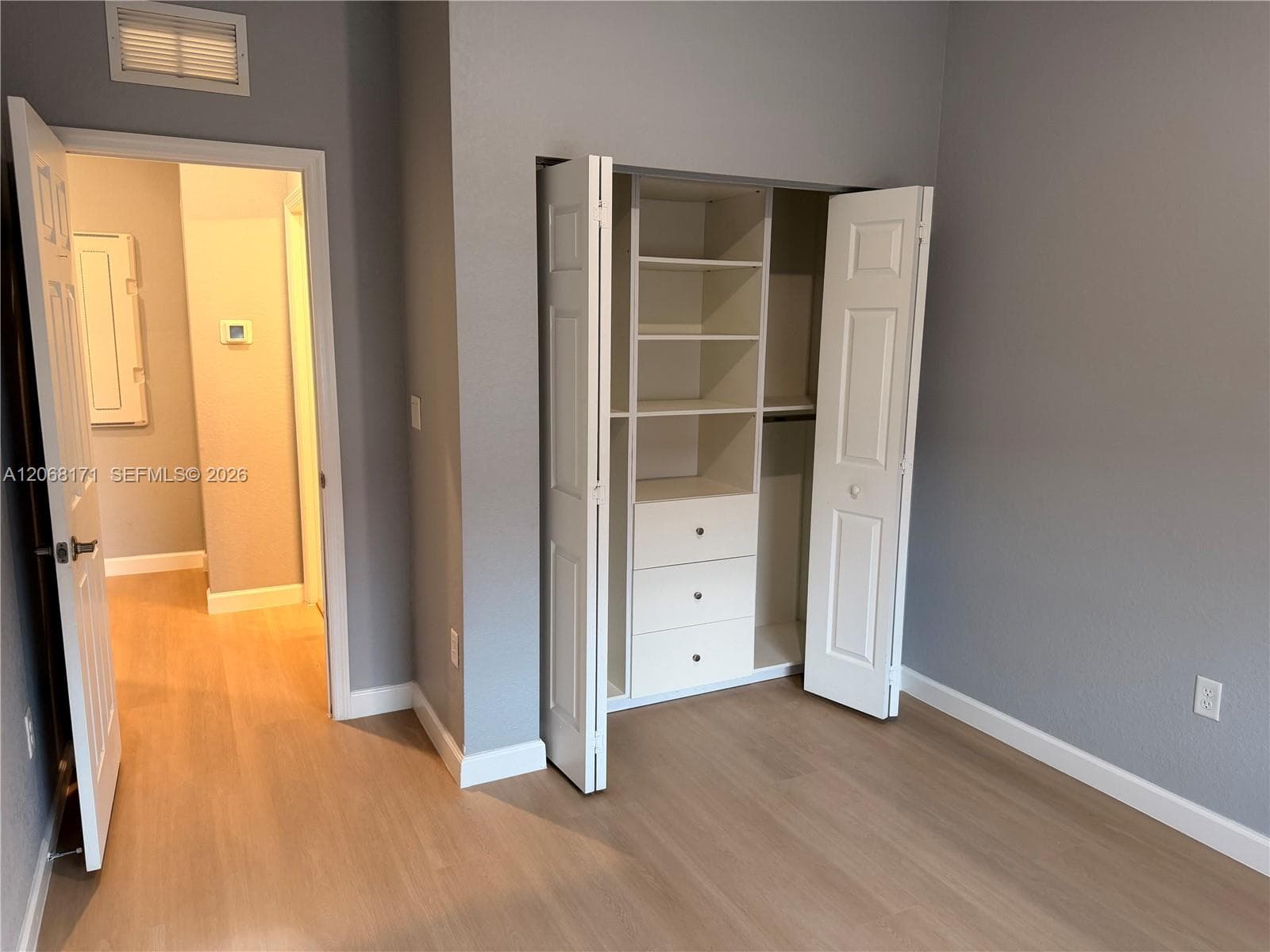 Interior space featuring wood-finish flooring, a built-in closet system with open shelving and three integrated drawers, and paneled swinging doors