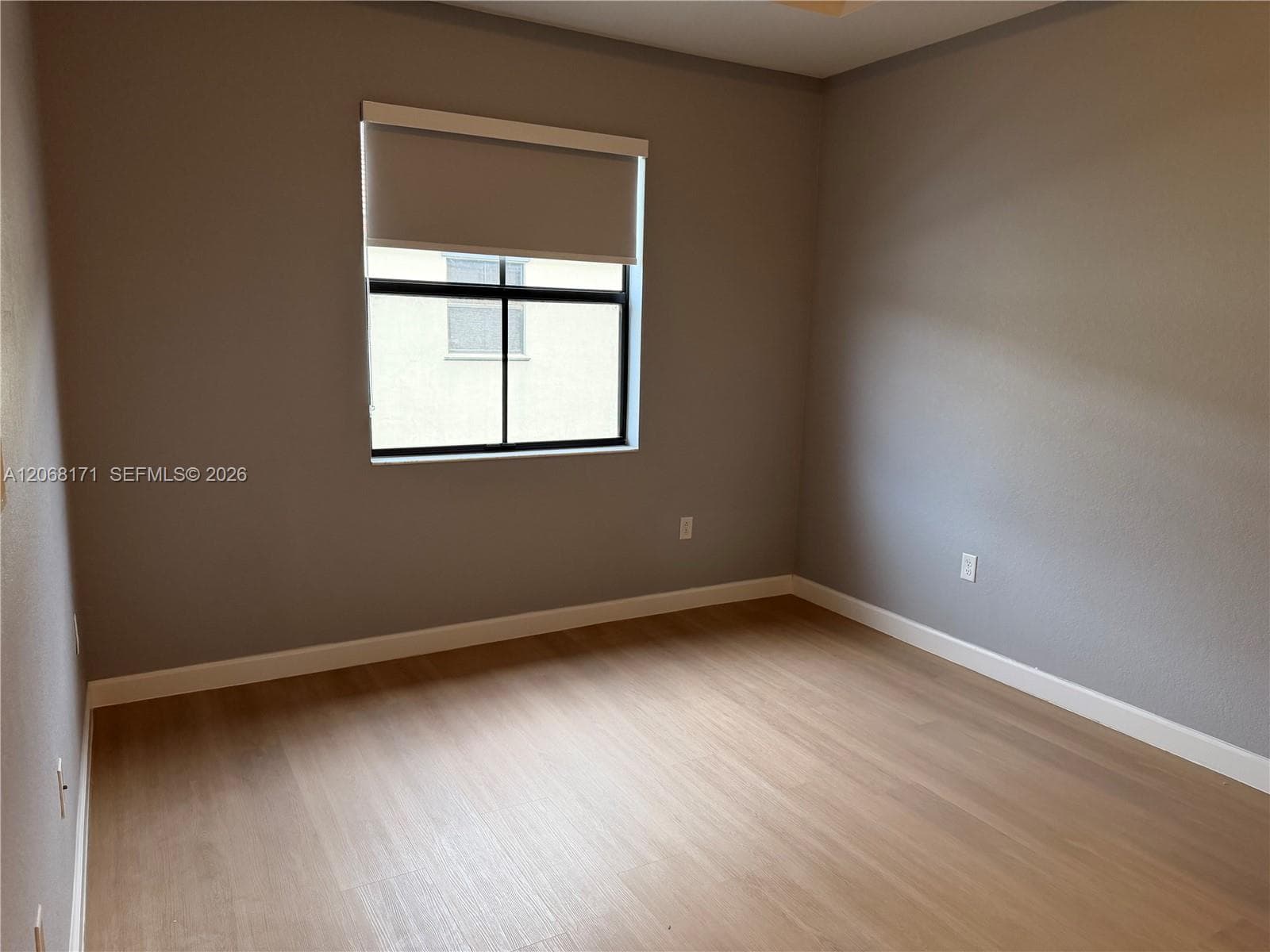 Neutral-toned interior featuring wood-finish flooring and a single-pane window with a roller shade