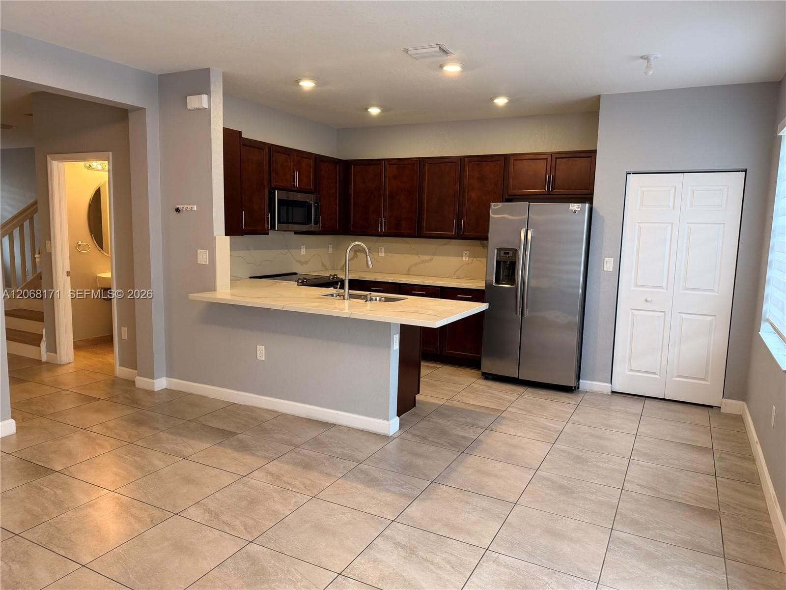 Kitchen featuring dark wood cabinetry, a stone-finish countertop, a stainless steel refrigerator, recessed lighting, and tile flooring