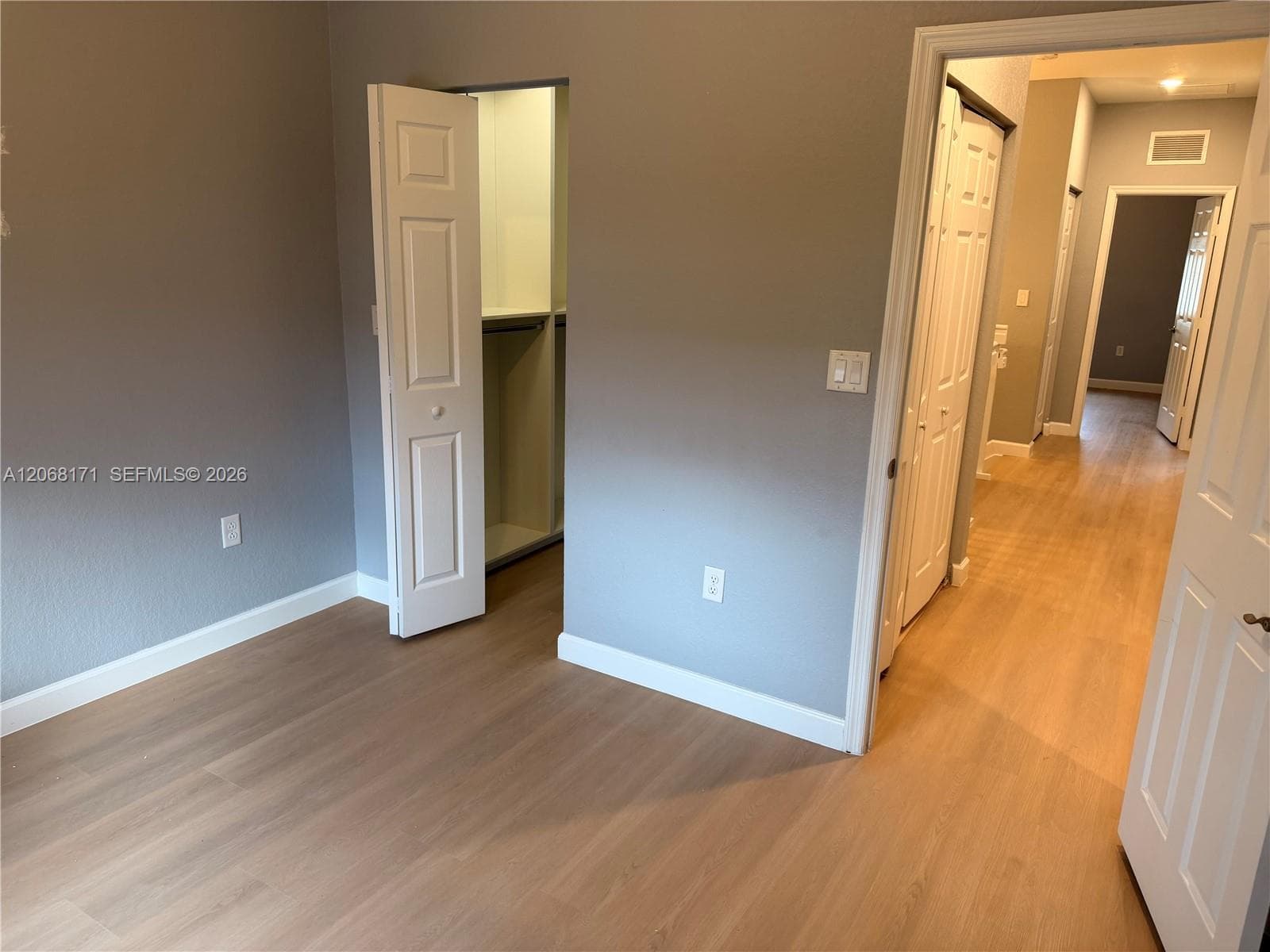 Interior space featuring wood-finish flooring, neutral wall tones, a built-in closet with multi-level shelving, and white six-panel interior doors