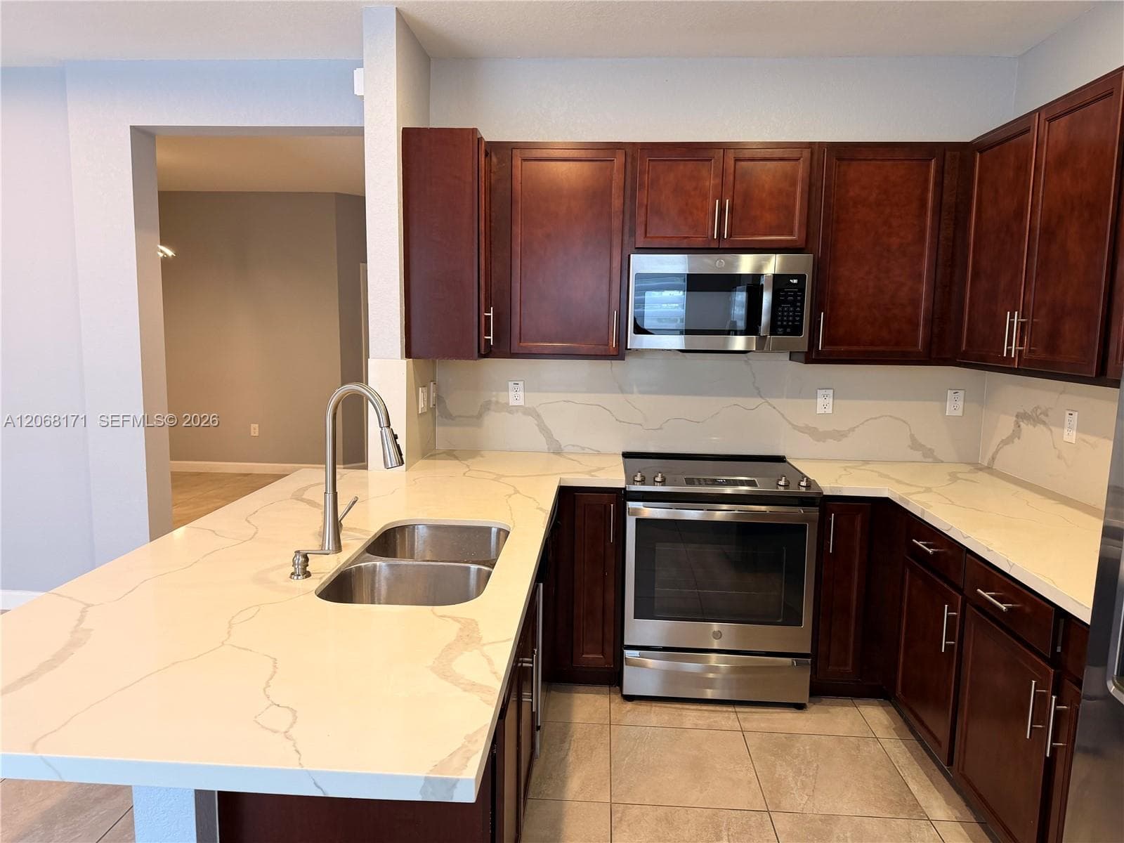 Kitchen featuring dark-toned cabinetry, stone-finish countertops with a matching full-height backsplash, a stainless steel dual-basin undermount sink, and stainless steel appliances