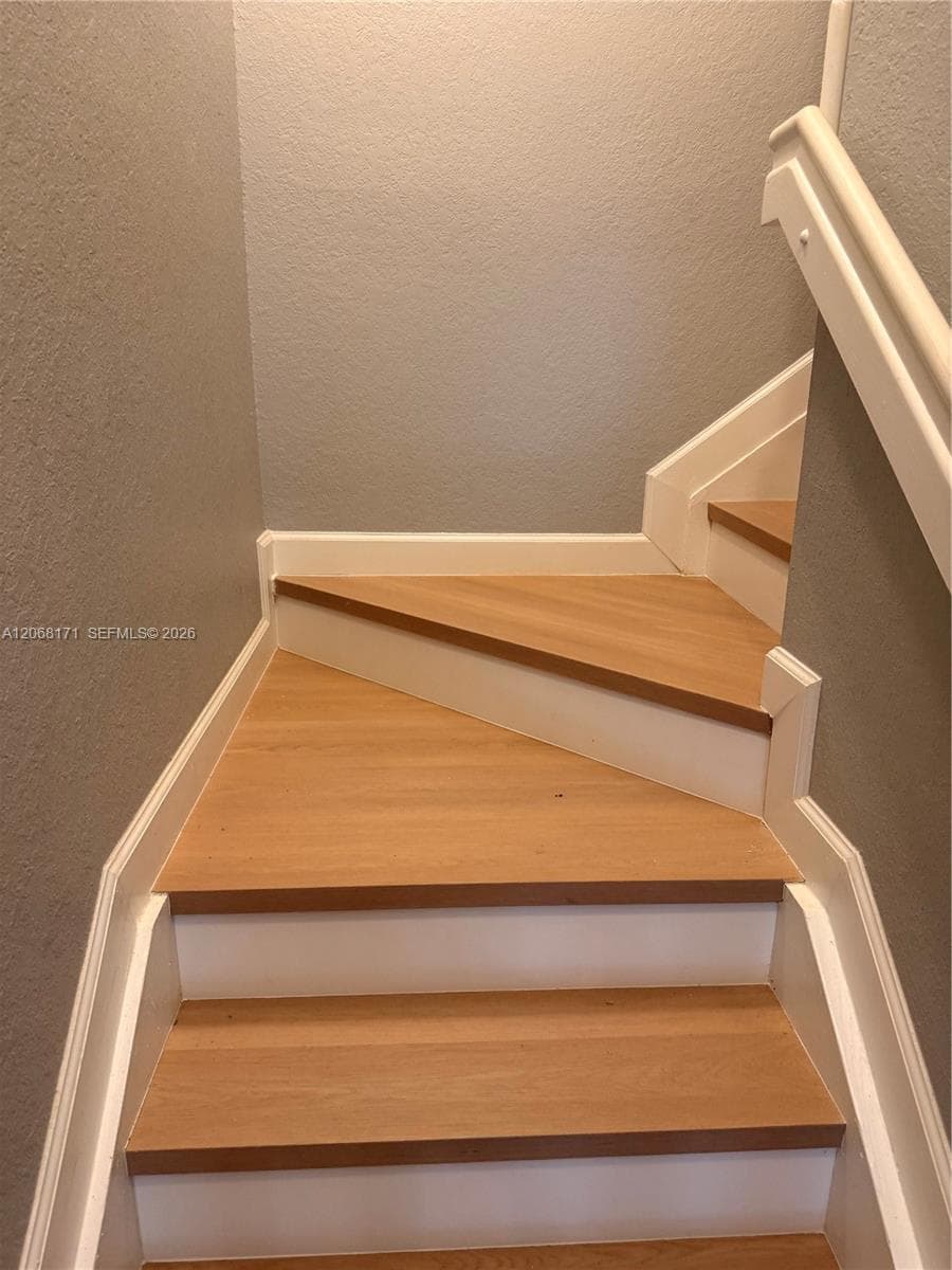 Staircase featuring wood-finish treads, white risers, and a matching handrail