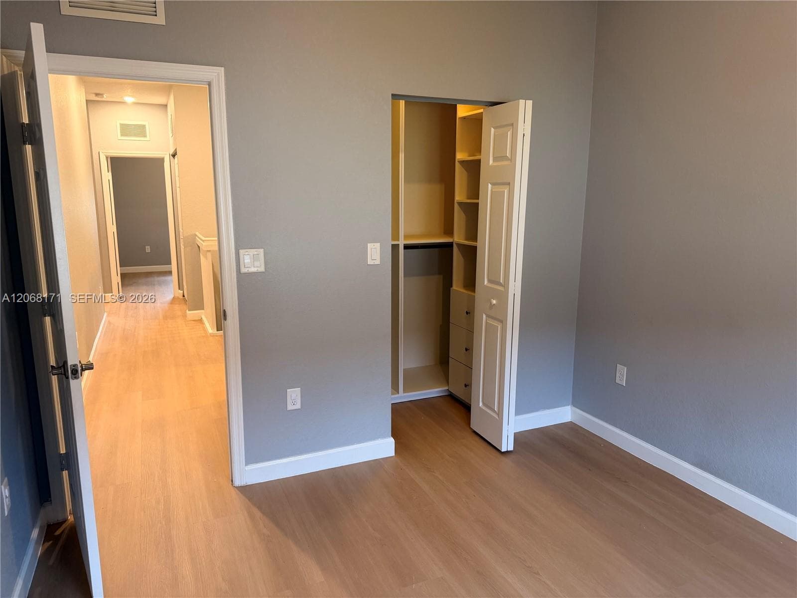 Room featuring wood-finish flooring, neutral wall paint, and a built-in closet system with integrated shelving and storage drawers