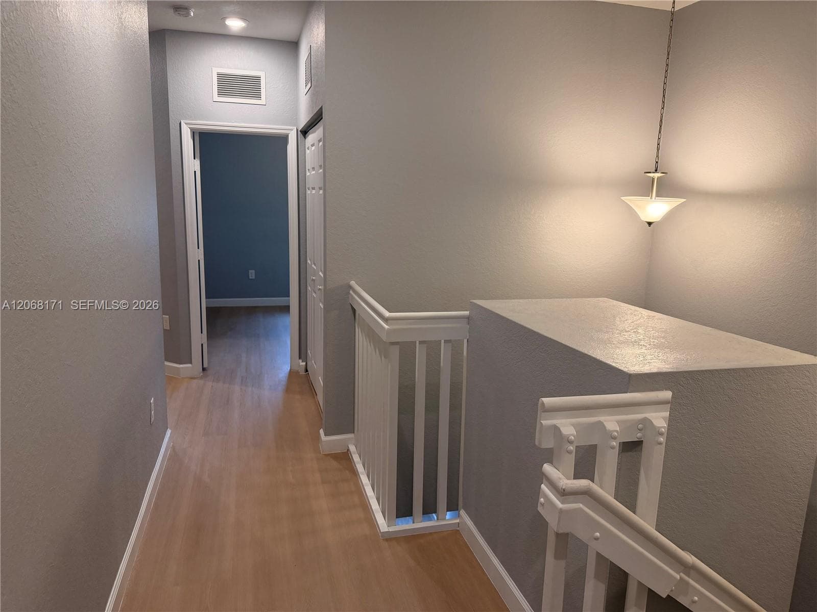 Hallway featuring wood-finish flooring, white spindle staircase railing, and a hanging pendant light fixture