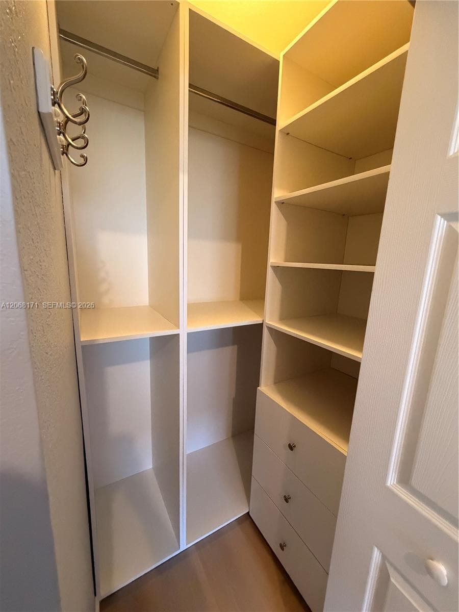 Walk-in closet featuring white built-in shelving, integrated hanging rods, a three-drawer storage unit, and a mounted wall hook fixture