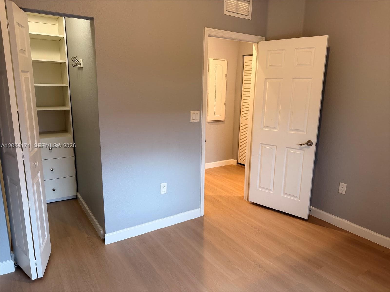 Room featuring wood-finish flooring, a built-in closet with multi-level shelving and drawers, and a six-panel door