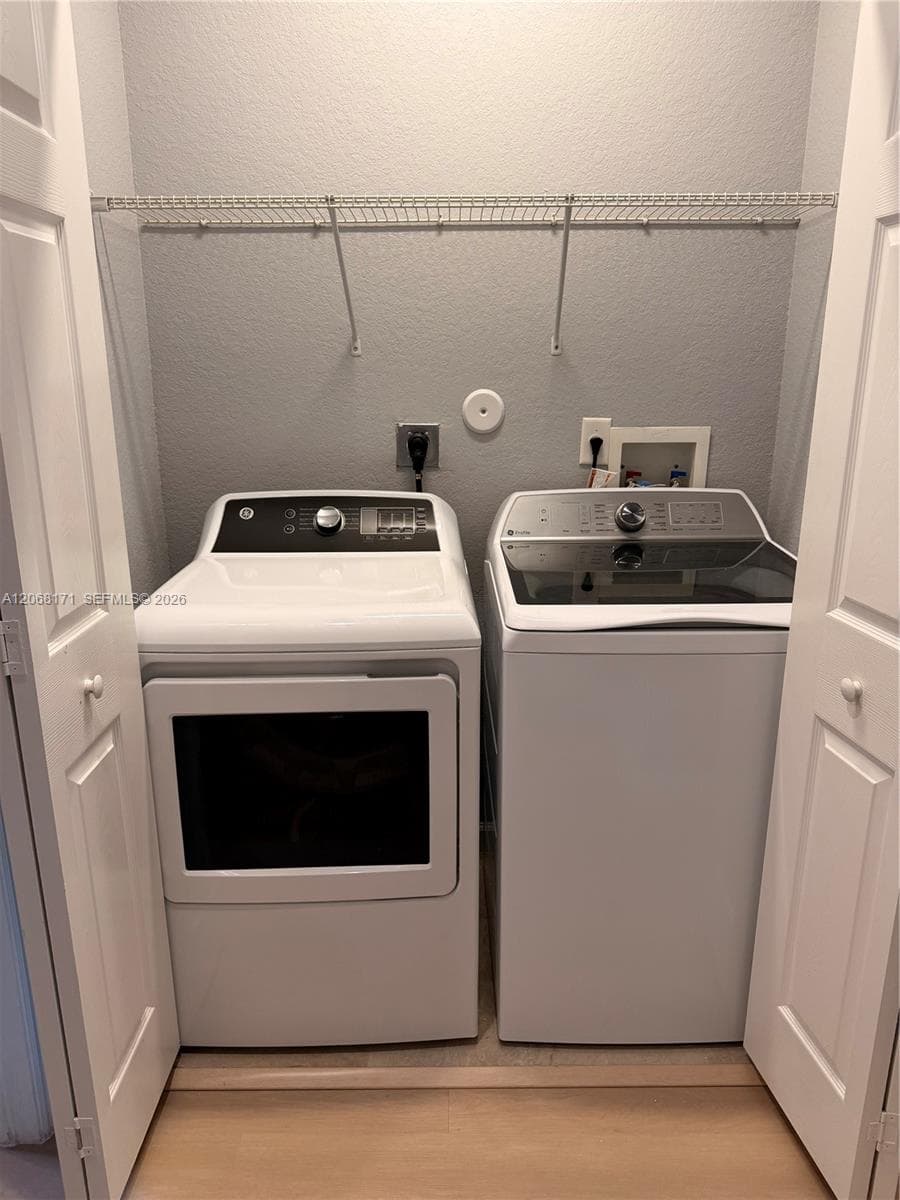 Laundry closet featuring bi-fold doors, white top-loading appliances, and an overhead wire storage shelf