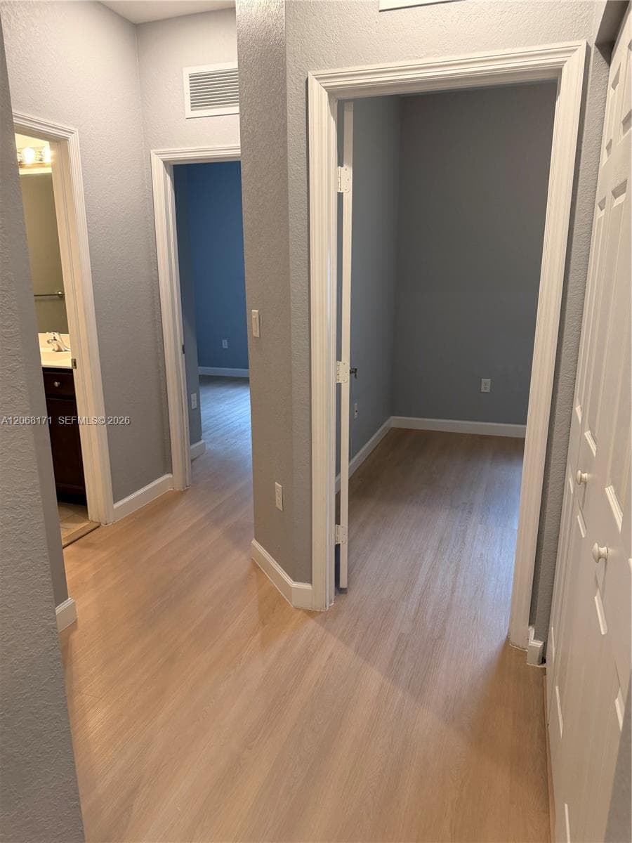 Hallway featuring light-toned wood-finish flooring, crisp white door casings, and multi-panel interior doors