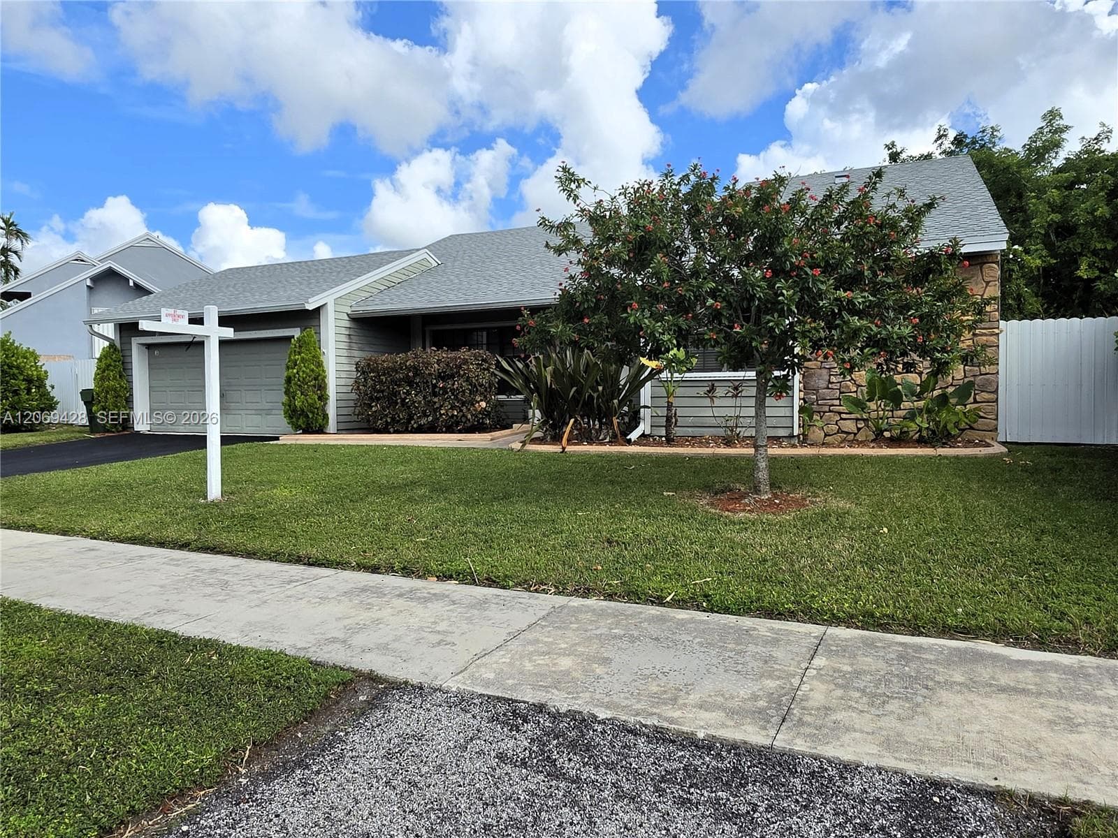 Single-story residence featuring a two-car garage, stone and siding exterior, and a white privacy fence