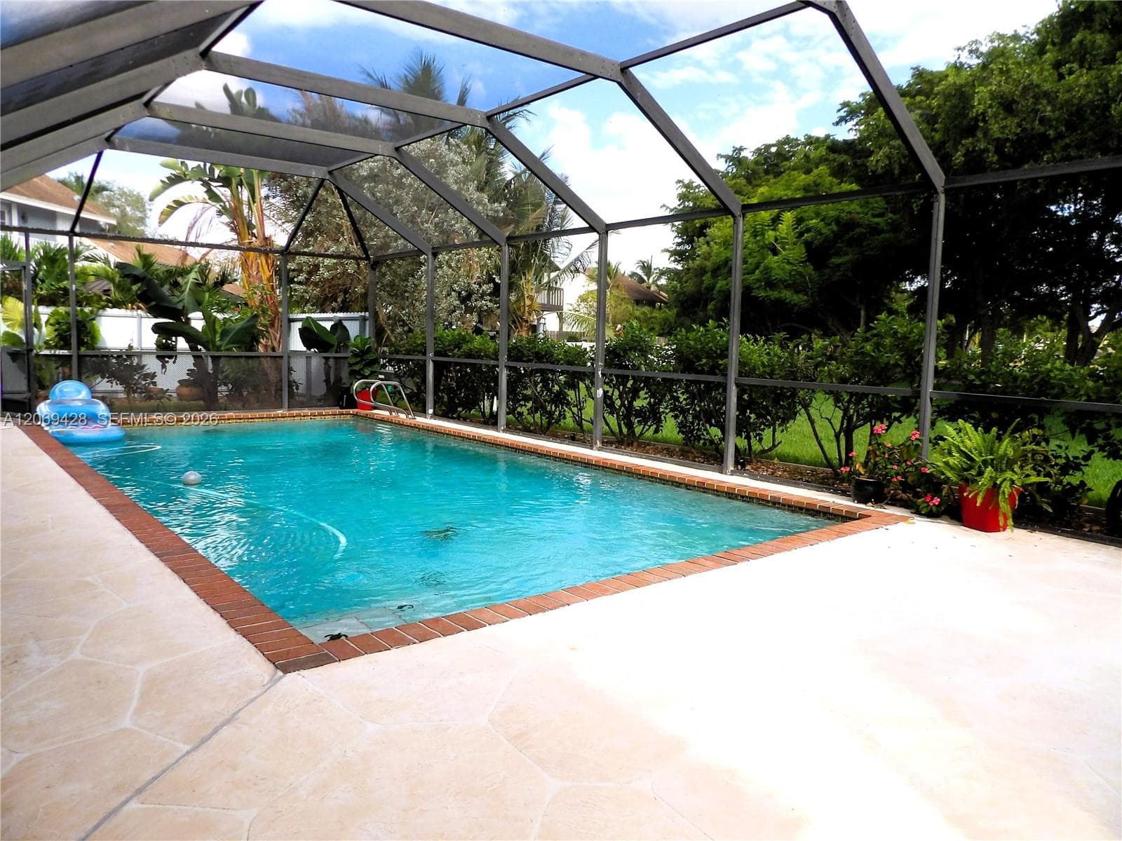 Screened enclosure with an in-ground swimming pool, brick coping, and a surrounding paver patio