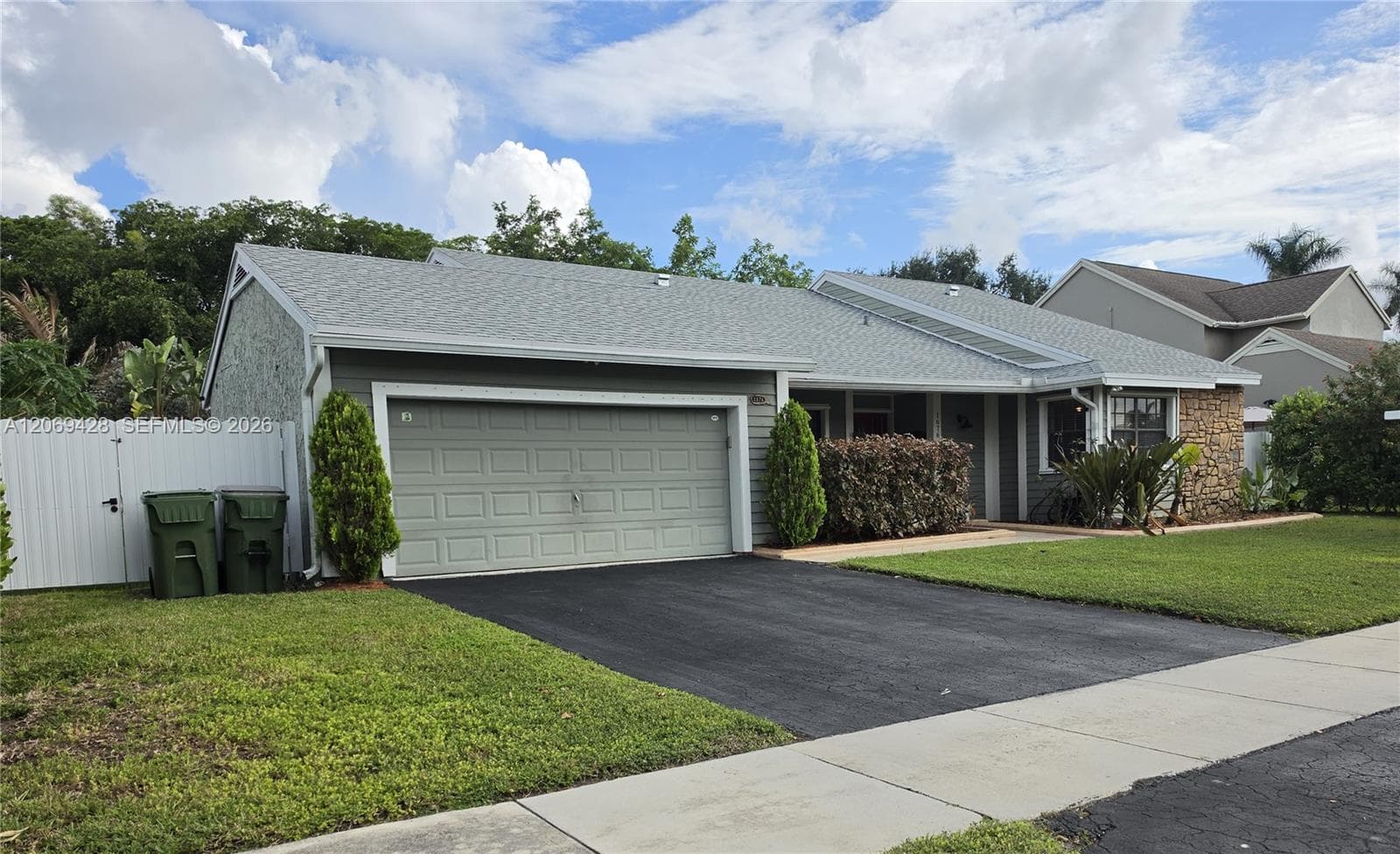 Attached two-car garage with a paved driveway, shingle roofing, and stone facade accents