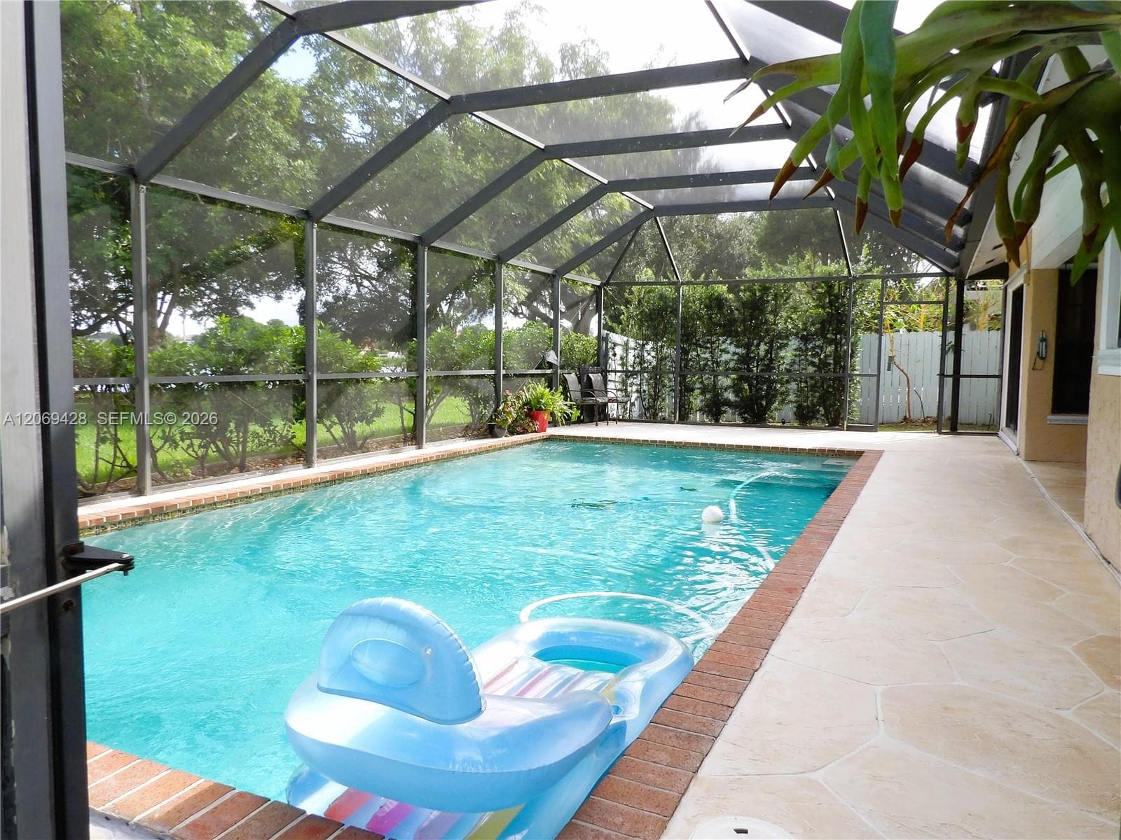 Screen-enclosed swimming pool featuring a brick coping, light-colored pool deck, and lush perimeter landscaping