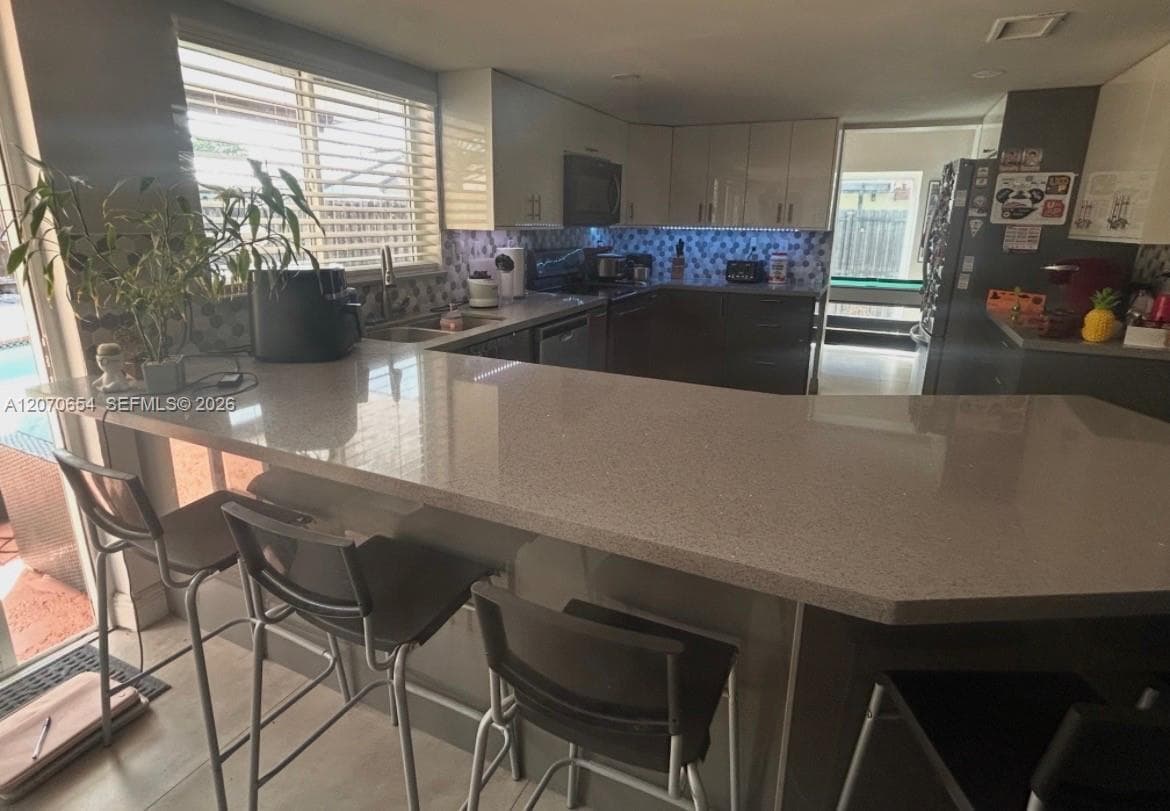 Spacious kitchen island with seating, glossy upper cabinetry, integrated sink, and tile backsplash