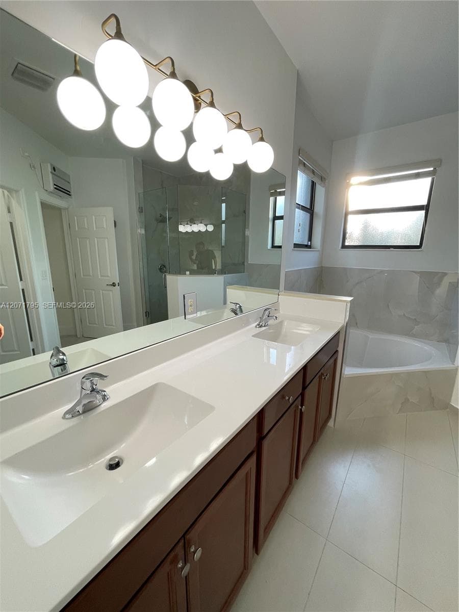 Dual-sink vanity with a solid-surface countertop, dark wood-finish cabinetry, large wall-mounted mirror, multi-globe light fixture, and corner soaking tub