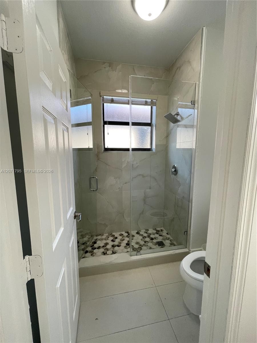Walk-in shower featuring floor-to-ceiling tile, a frameless glass enclosure, pebble-stone shower floor, and a wall-mounted shower head, complemented by large-format tile flooring