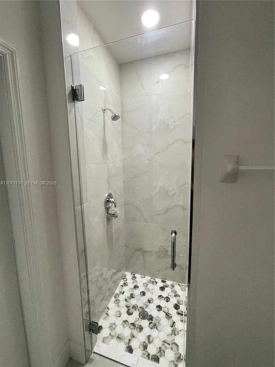 Walk-in shower featuring large-format stone-finish wall tile, a frameless glass door, a metallic hand-held shower head, and decorative hexagonal floor tiling
