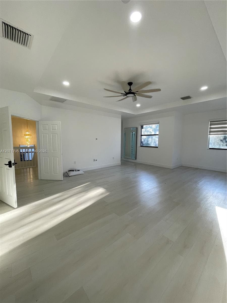 Tray ceiling with recessed lighting, wood-finish flooring, and a multi-blade ceiling fan