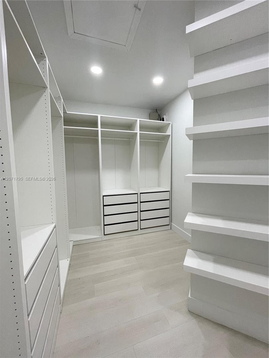 Custom walk-in storage featuring floor-to-ceiling white shelving, integrated drawer banks, hanging rods, and light-toned wood-finish flooring