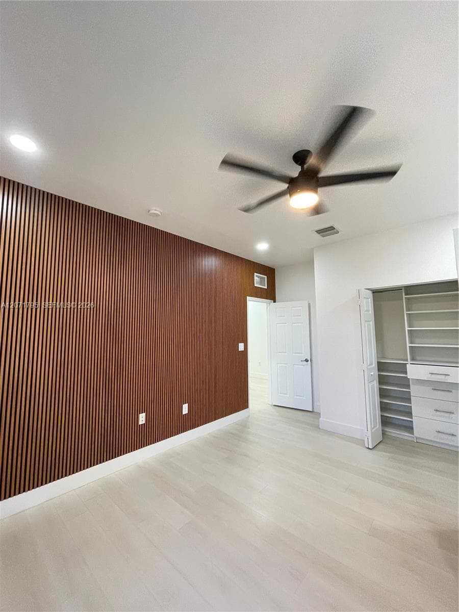 Interior space featuring a slatted wood-finish accent wall, light-toned wood-finish flooring, recessed lighting, and a modern ceiling fan with an integrated light fixture