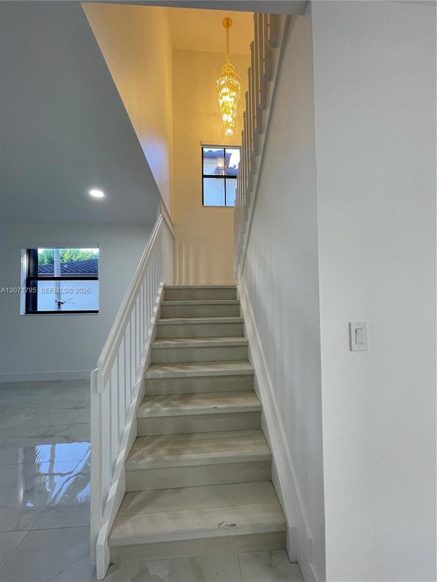 Staircase featuring white balusters and wood-finish treads, complemented by a multi-tiered crystal chandelier, recessed lighting, and large-format tile flooring