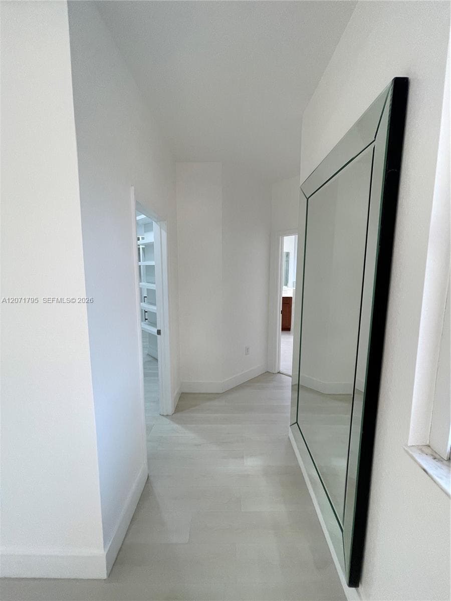 Hallway featuring neutral-toned wood-finish flooring and stark white walls