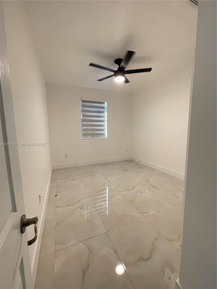 Large-format neutral tile flooring, matte black ceiling fan with integrated lighting, and window with installed dual-shade roller blinds