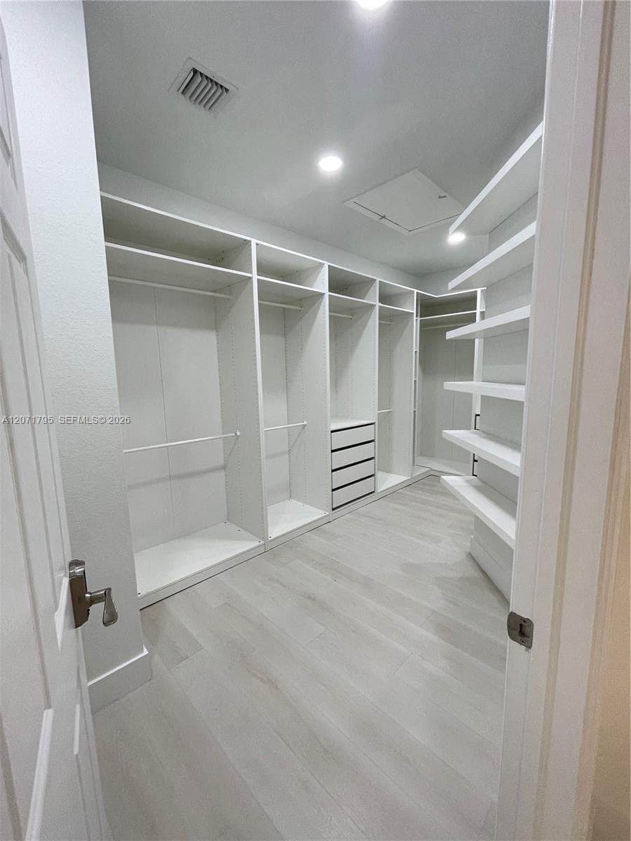 Walk-in closet featuring floor-to-ceiling white custom built-in cabinetry, integrated drawer storage, open shelving, and wood-finish flooring
