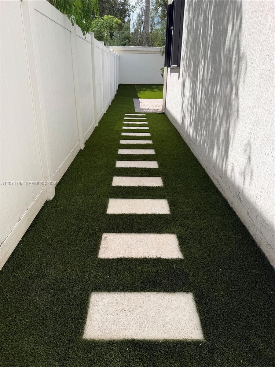 Side yard featuring synthetic turf, concrete paver stones, and white vinyl privacy fencing