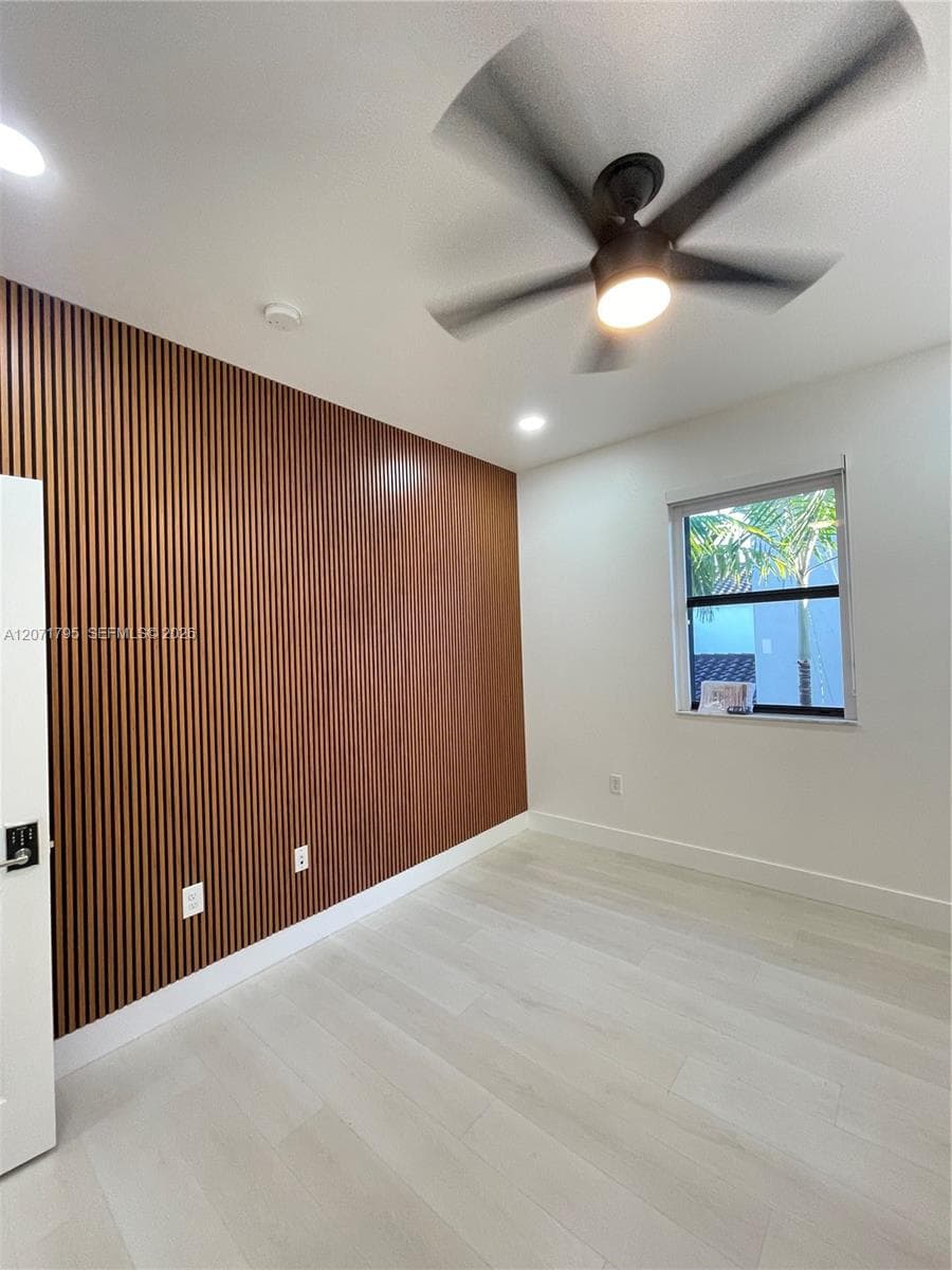Vertical wood-slat accent wall, light-toned wood-finish flooring, matte black ceiling fan with integrated lighting, and recessed overhead lighting