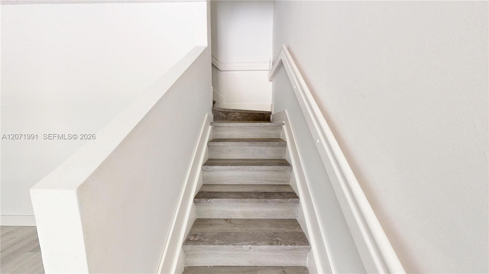 Staircase featuring wood-finish treads, white painted walls, and a matching white handrail