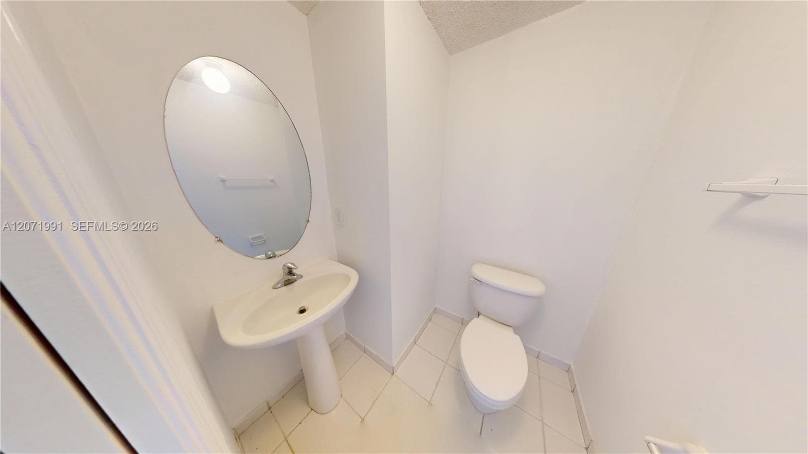 Powder room featuring a pedestal sink, wall-mounted oval mirror, ceramic tile flooring, and a standard toilet