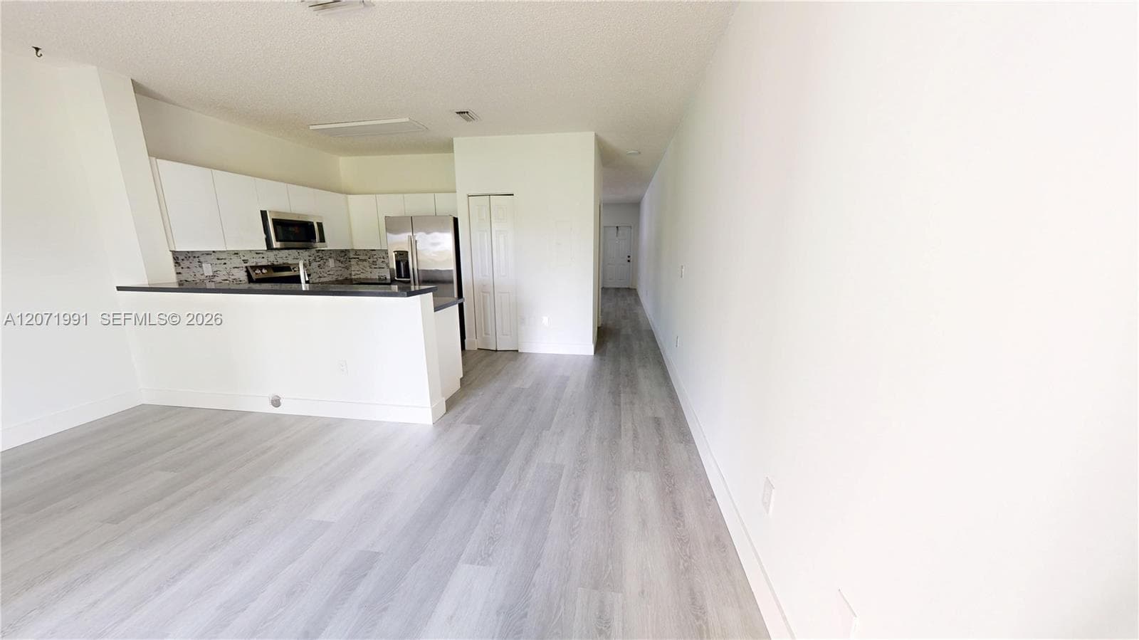 Kitchen featuring a breakfast bar, white cabinetry, stainless steel appliances, a mosaic tile backsplash, and wood-finish flooring