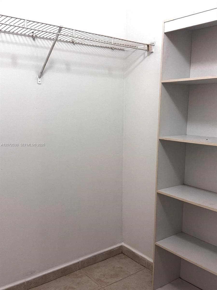 Walk-in closet featuring built-in floor-to-ceiling shelving, overhead wire racking, and tiled flooring