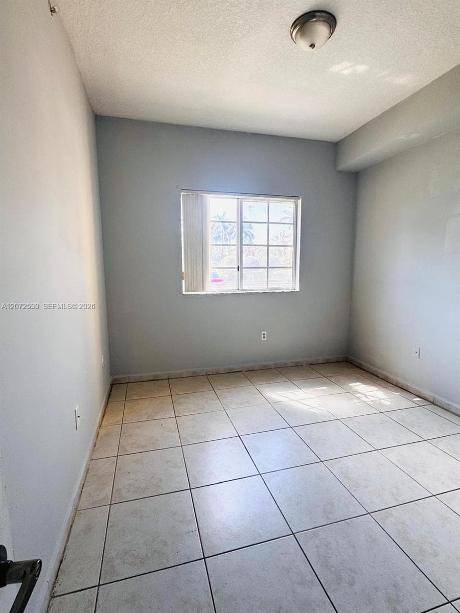 Interior room featuring neutral-toned tile flooring, light-colored walls, a grid-patterned window, and a flush-mount ceiling light