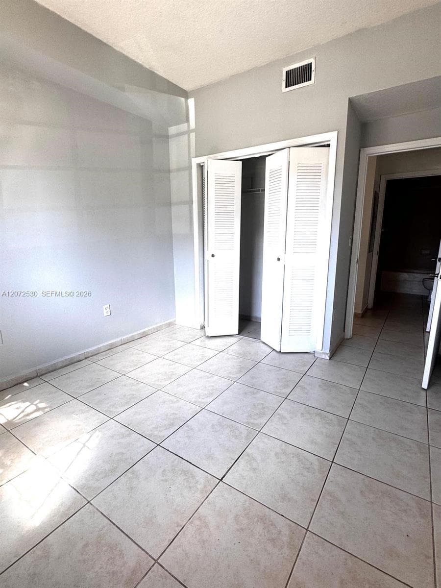 Neutral-toned room featuring large-format ceramic tile flooring, vaulted ceilings, and a closet with white louvered bifold doors