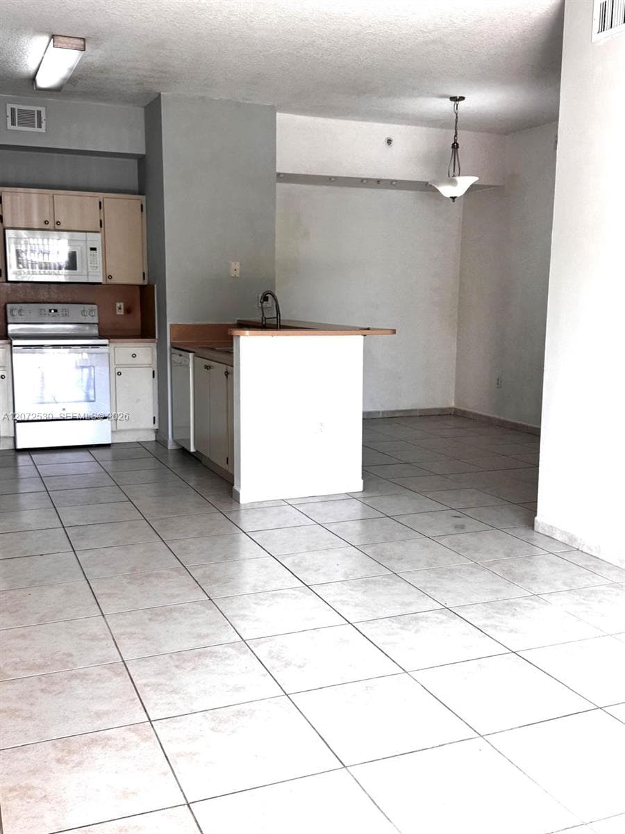 Kitchen featuring cabinetry with light-finish fronts, stone-surface countertop, stainless steel appliance package, and ceramic tile flooring